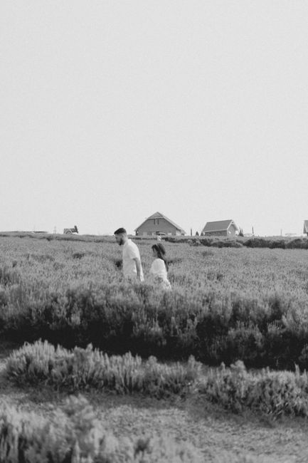 A couple enjoys a peaceful walk in expansive countryside fields with houses in the distance.