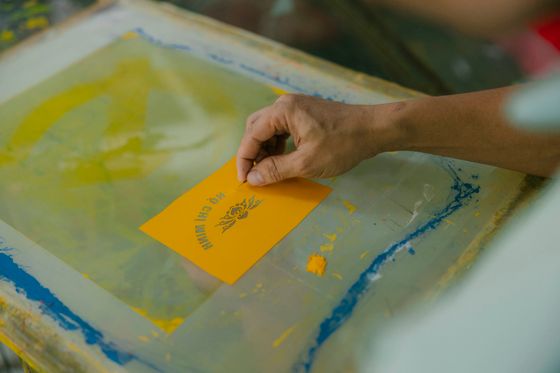 Hand pulling a screen print onto a yellow card — photo by HONG SON on Pexels