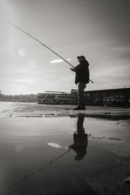 Free A fisherman casts his line at İstanbul's waterfront, capturing the serene morning ambiance. Stock Photo