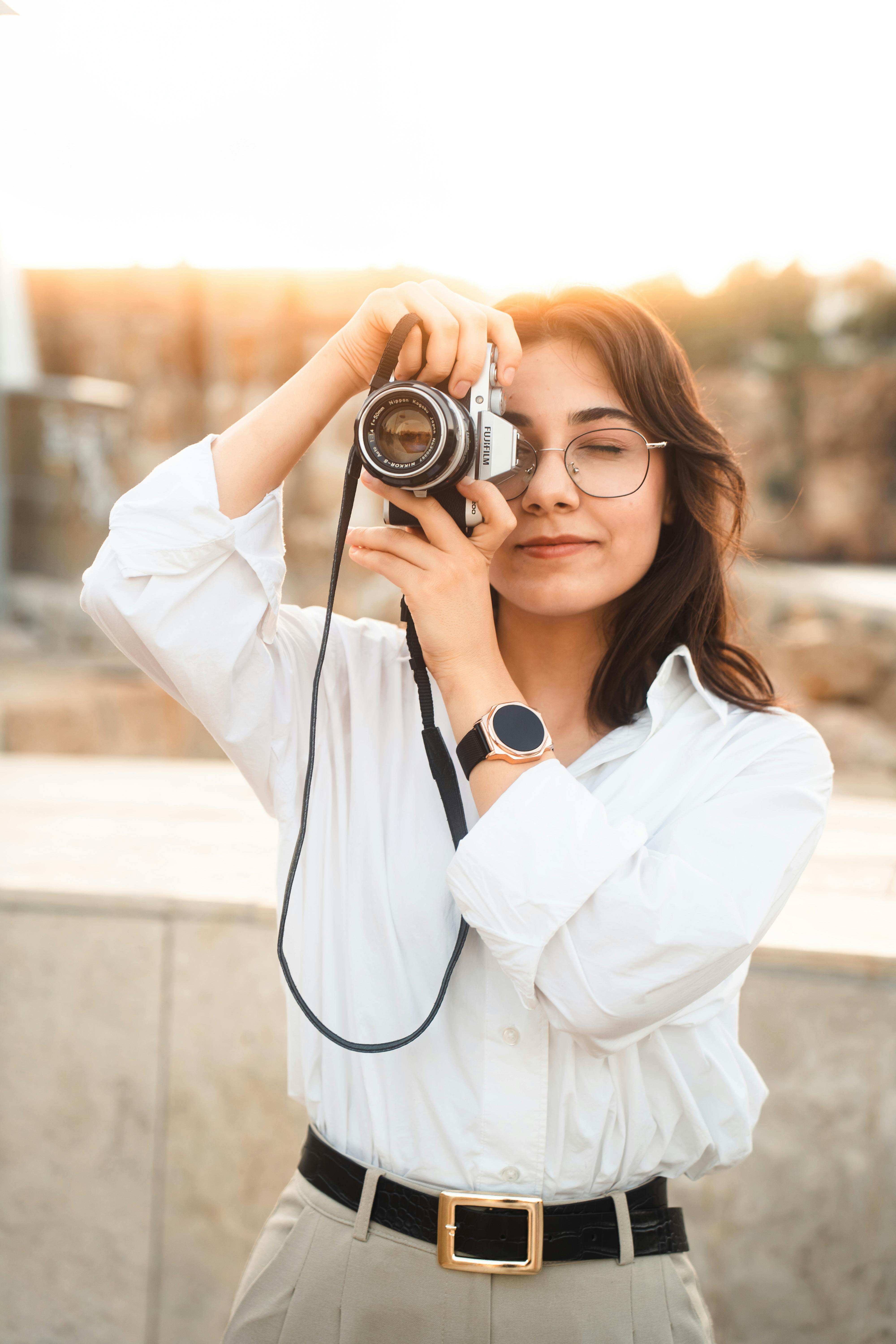 A young woman capturing moments with a vintage camera during sunset outdoors.