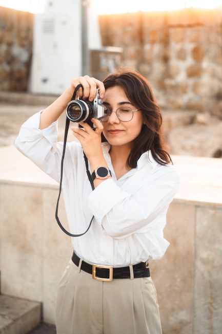 Smiling woman photographing in urban setting with vintage camera. Stylish and casual scene.