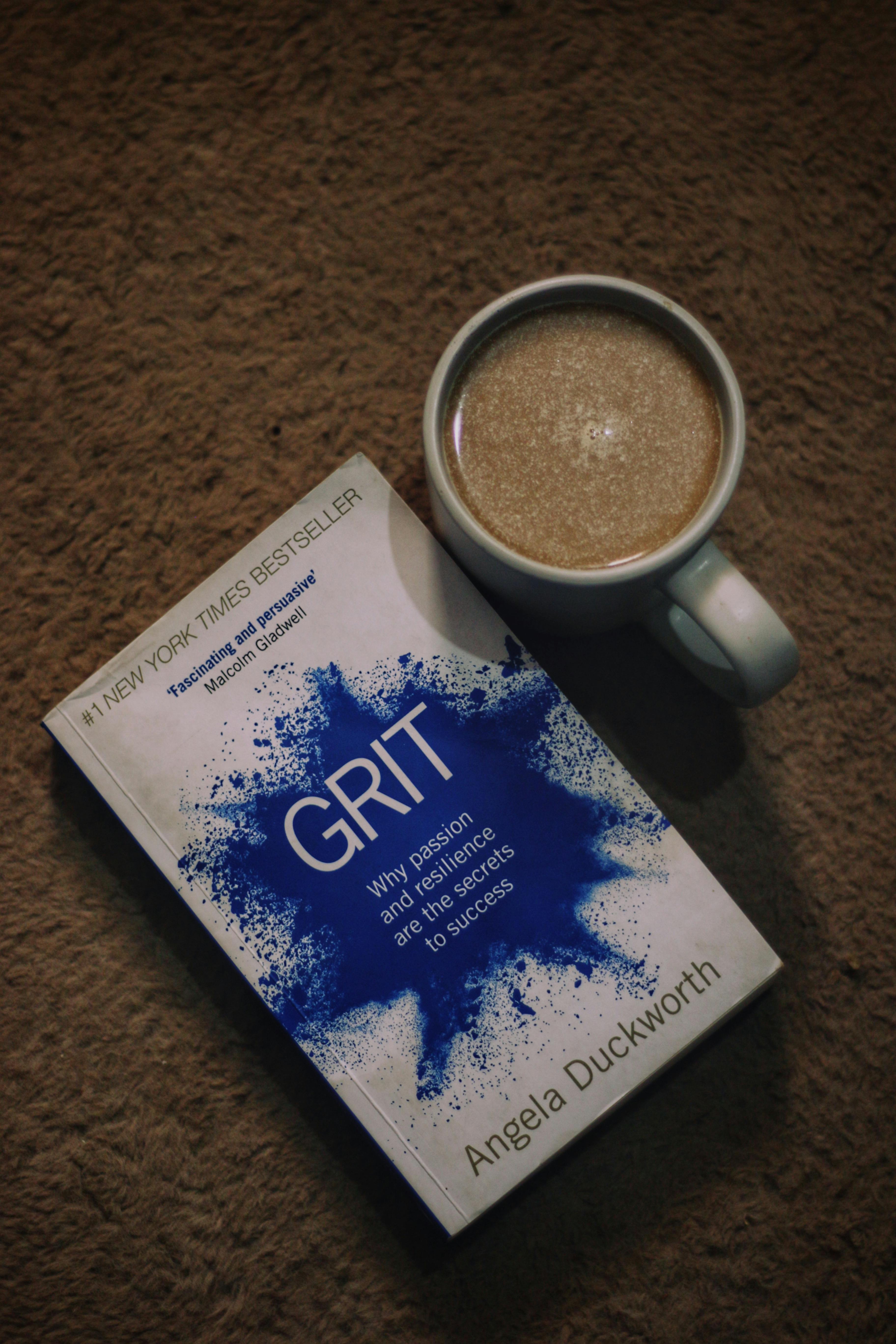 A cup of coffee alongside the book 'Grit' on a textured carpet, creating a cozy reading atmosphere.