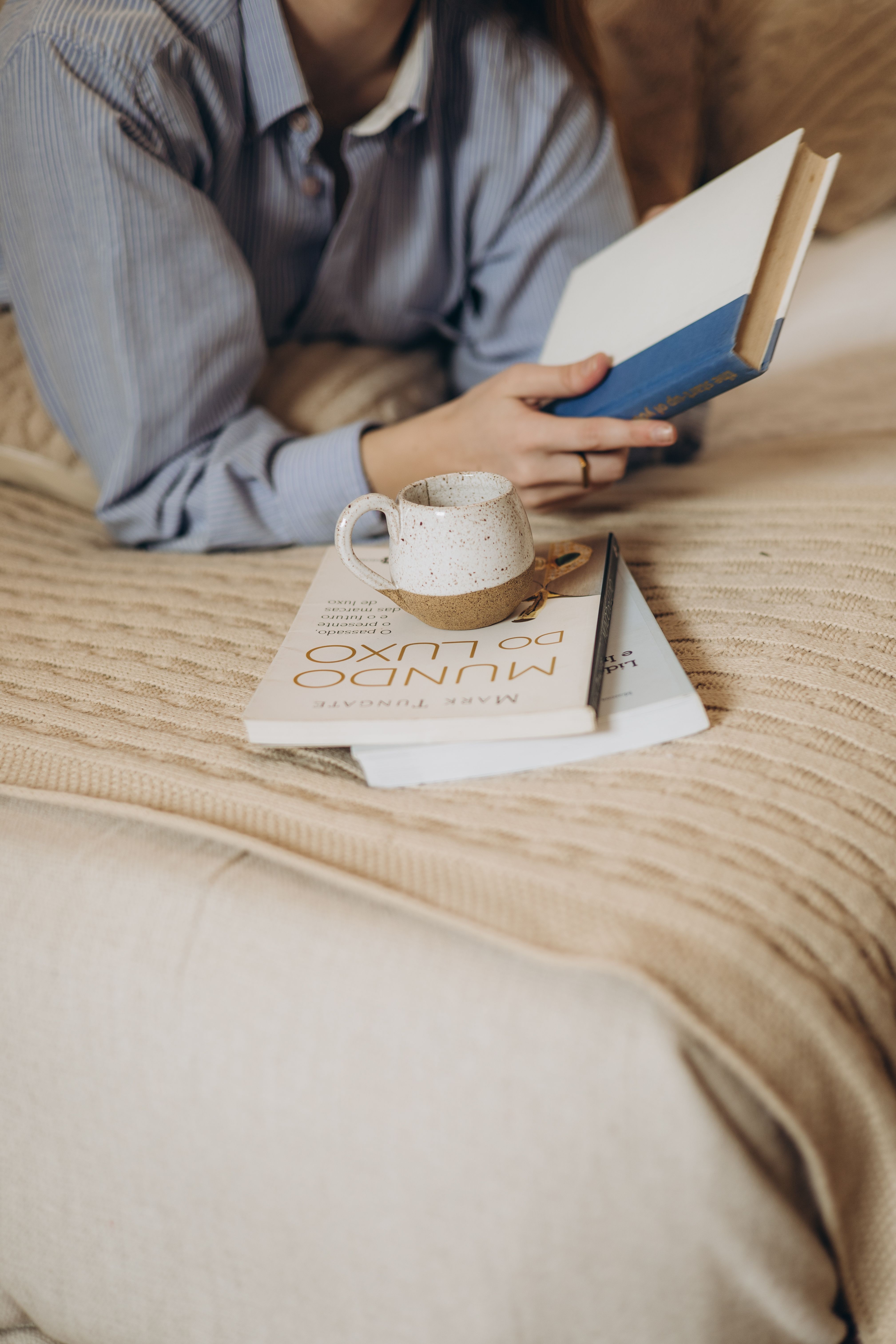 Woman reading a book in a cozy setting with coffee and books nearby.