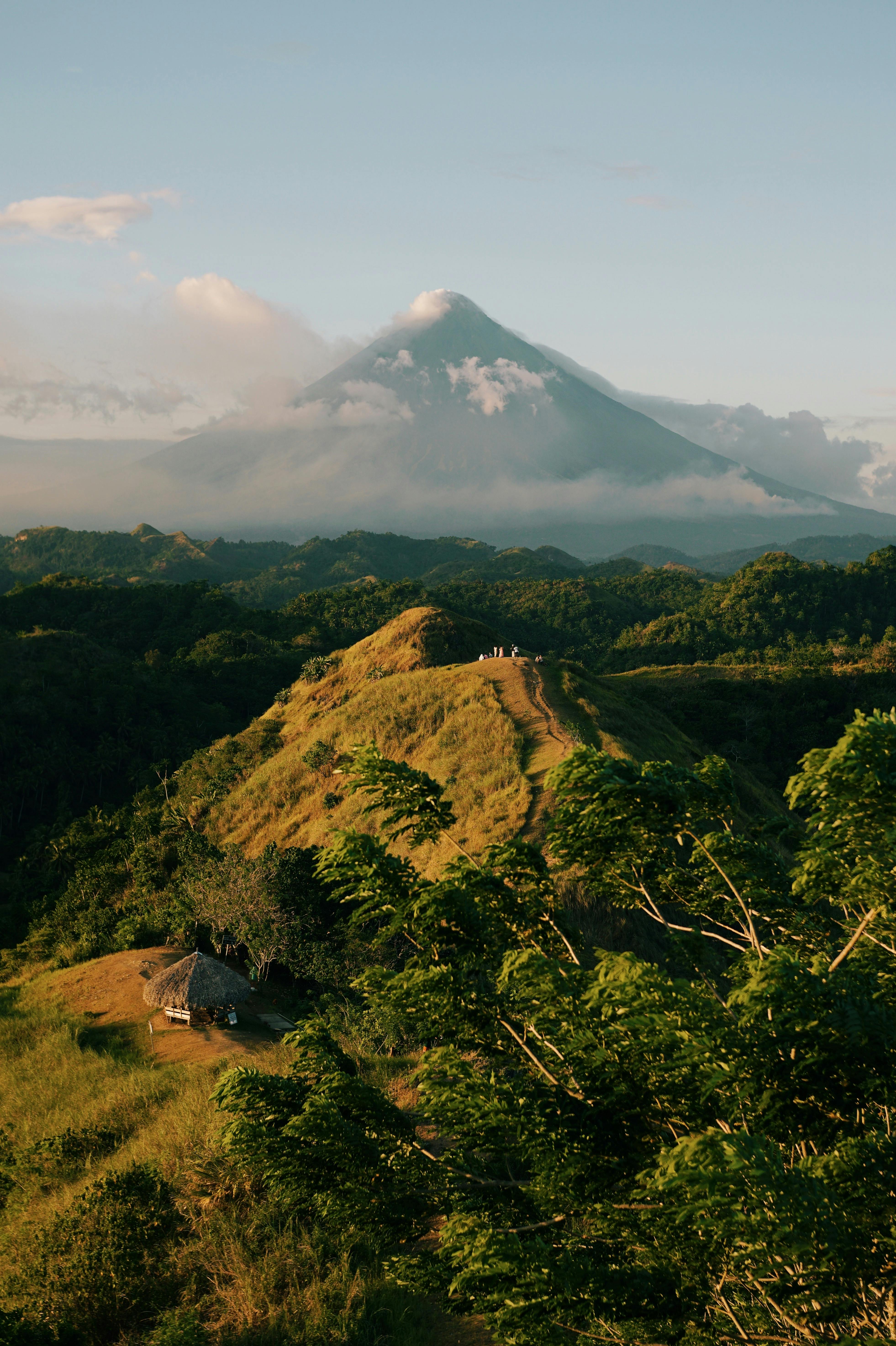 Lush green hills lead to a majestic volcano peak under clear skies.