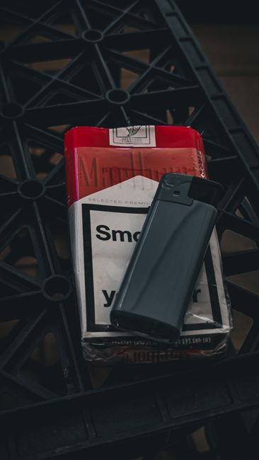 Close-up of a red and white cigarette pack with a black lighter on a textured surface.