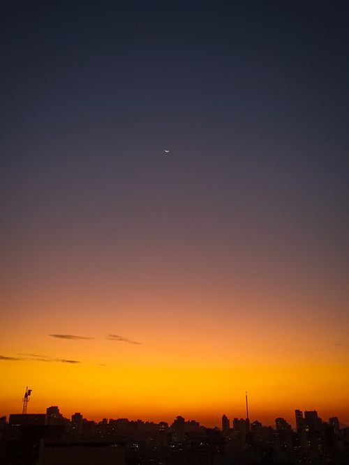 Free Stunning São Paulo skyline silhouetted against a vivid sunset with a crescent moon. Stock Photo