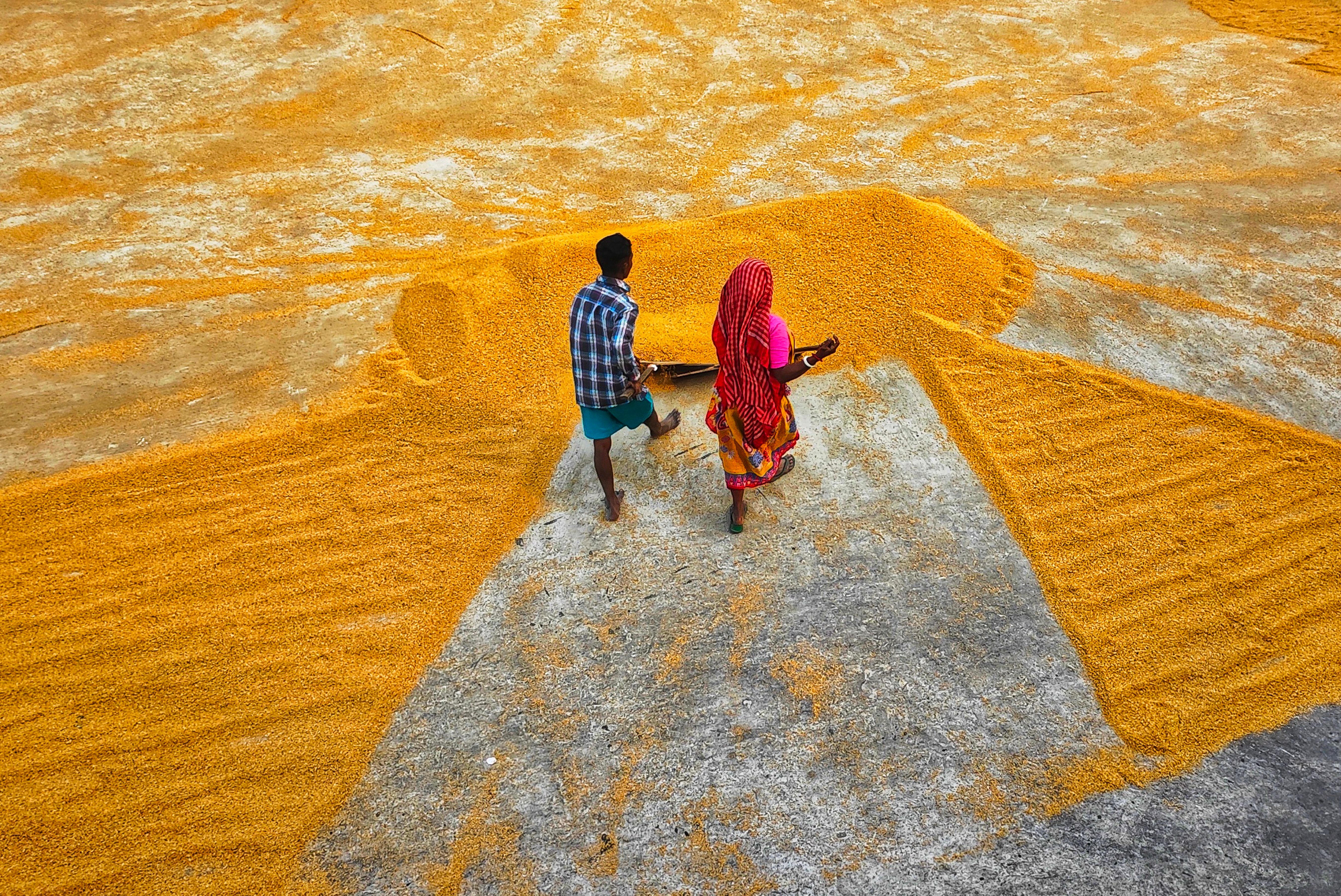 Aerial view of two workers spreading grains outdoors in Habra, India.