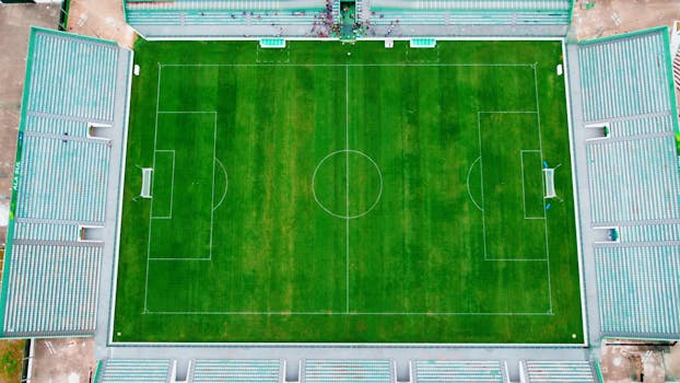 Drone shot of an empty soccer stadium in Brasília, featuring lush green field and seating areas.