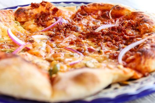 Free Close-up of a cheesy pizza topped with pepperoni, red onions, and spices, freshly baked. Stock Photo