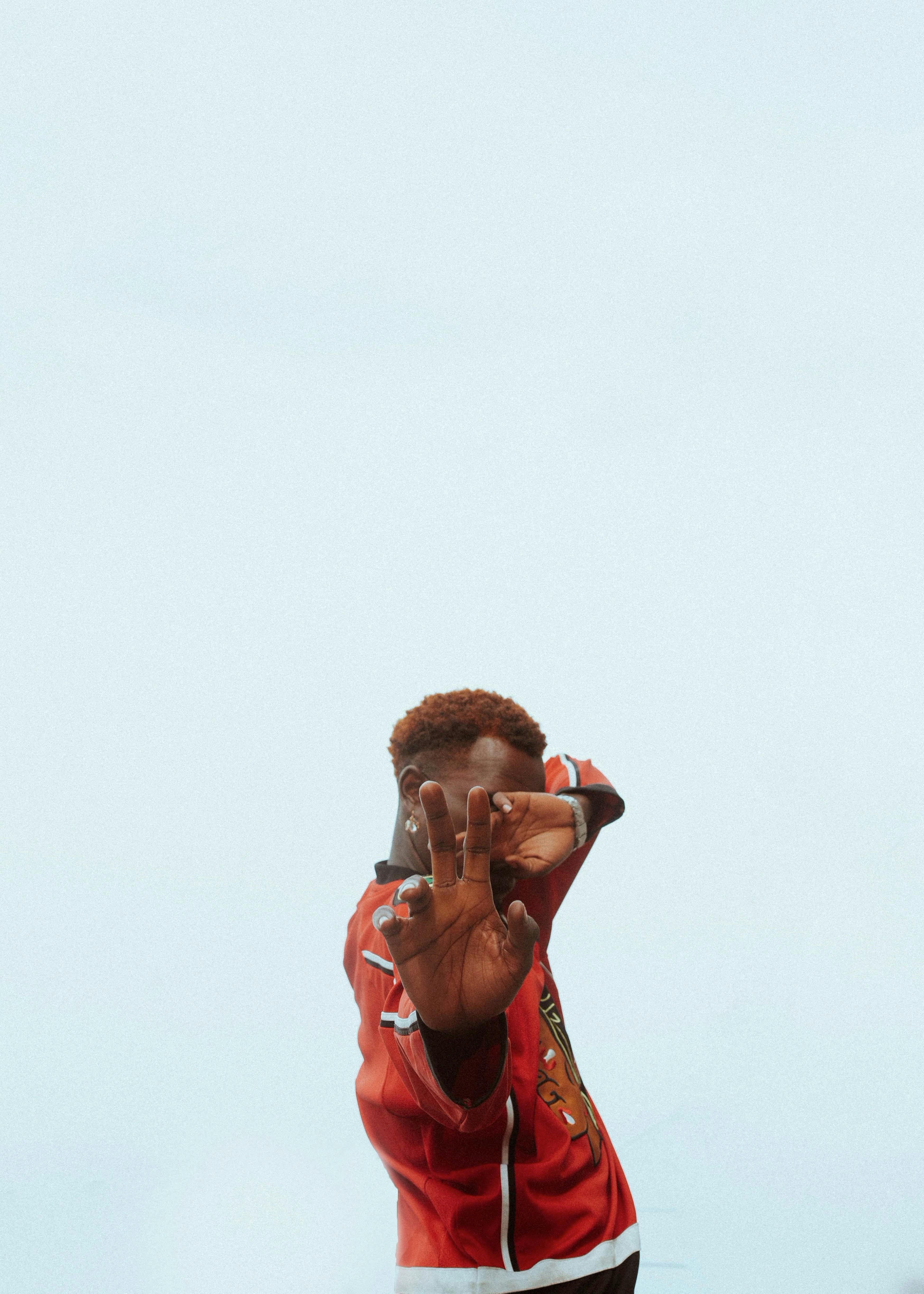 Free A young man in a red jacket poses creatively against a clear sky background. Stock Photo