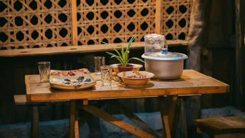 A rustic dining table set with plates, bowls, and a potted plant, creating a cozy indoor atmosphere.