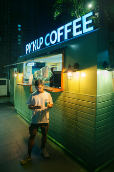 Man enjoying coffee at a pickup kiosk in the city at night.