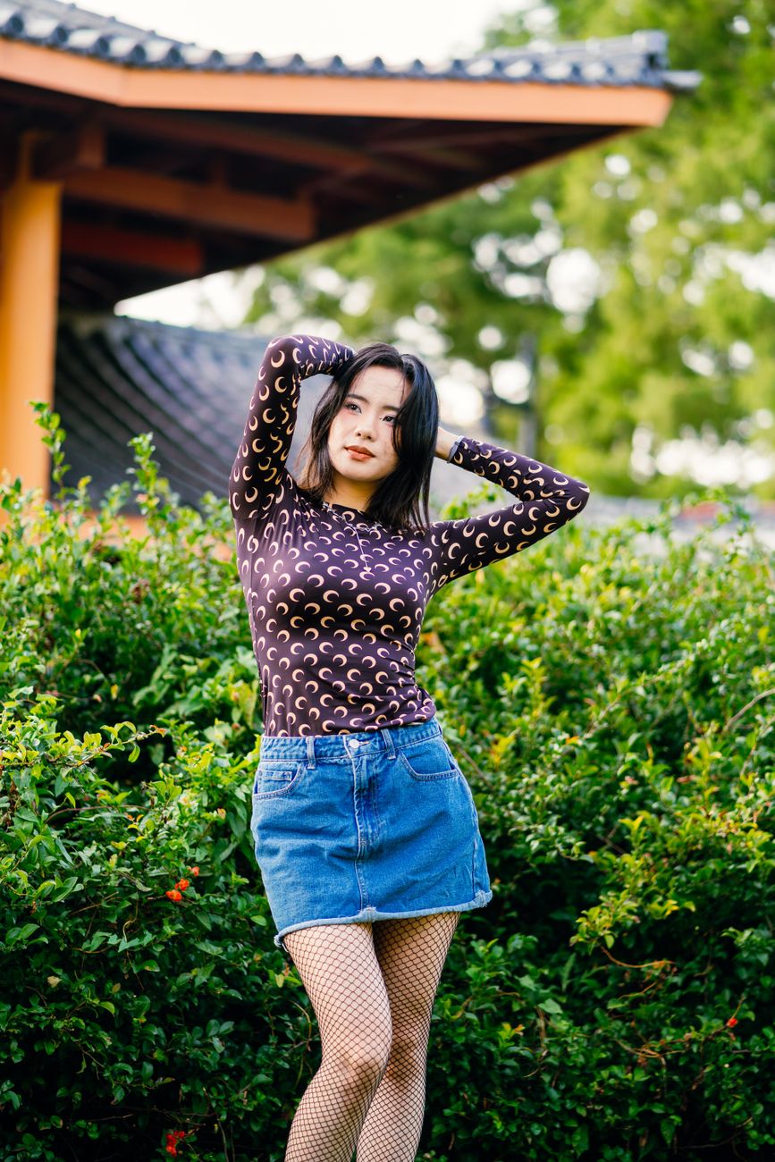 Woman posing outdoors with Asian architecture background, showcasing fashion and style.