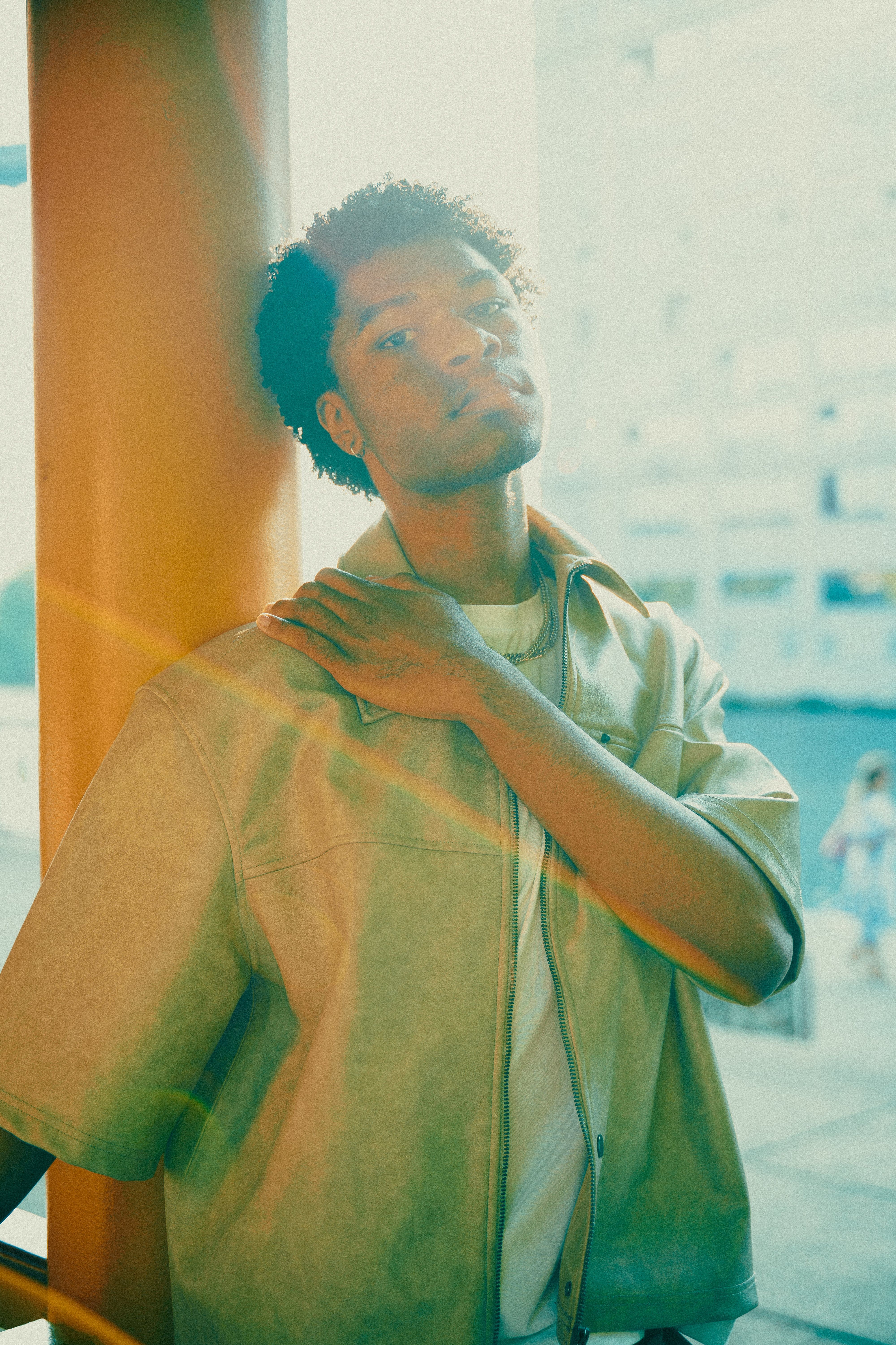 Fashionable young man poses outdoors with sunlight. Urban vibe and trendy style.