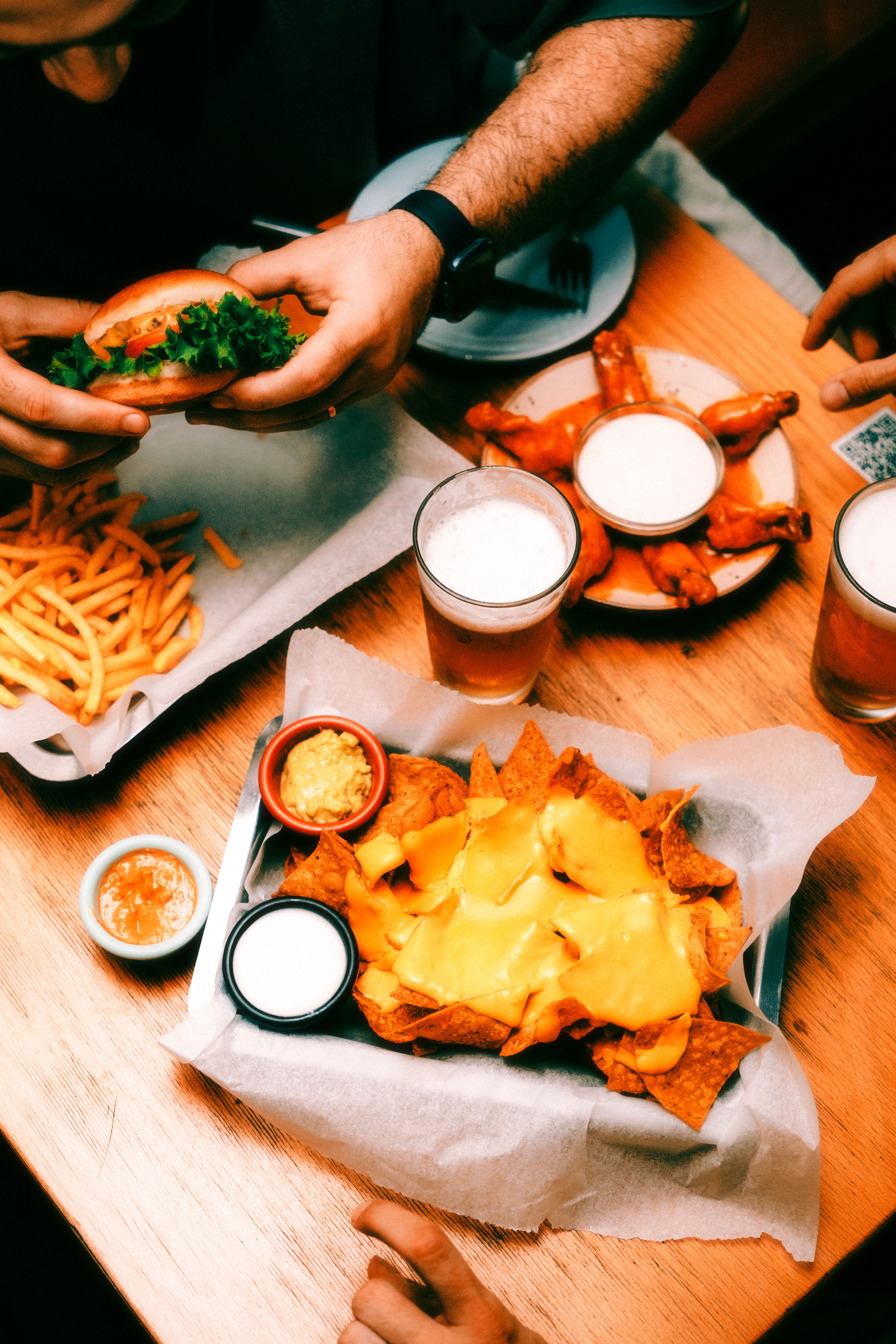 Vibrant dinner scene featuring nachos, burgers, fries, and craft beer in a cozy restaurant setting.