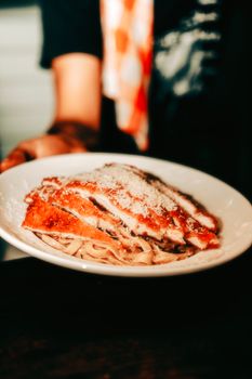 A mouthwatering plate of chicken parmesan over pasta served in a warm restaurant environment.