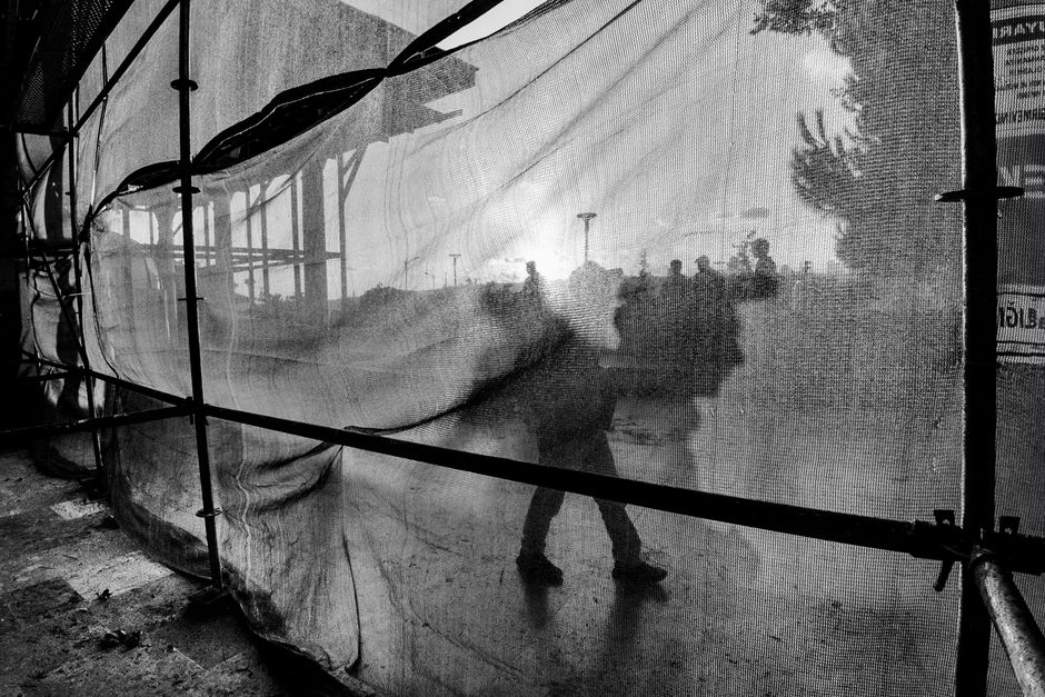 Silhouetted figures cast abstract shadows through a translucent fabric, creating a moody black and white scene.