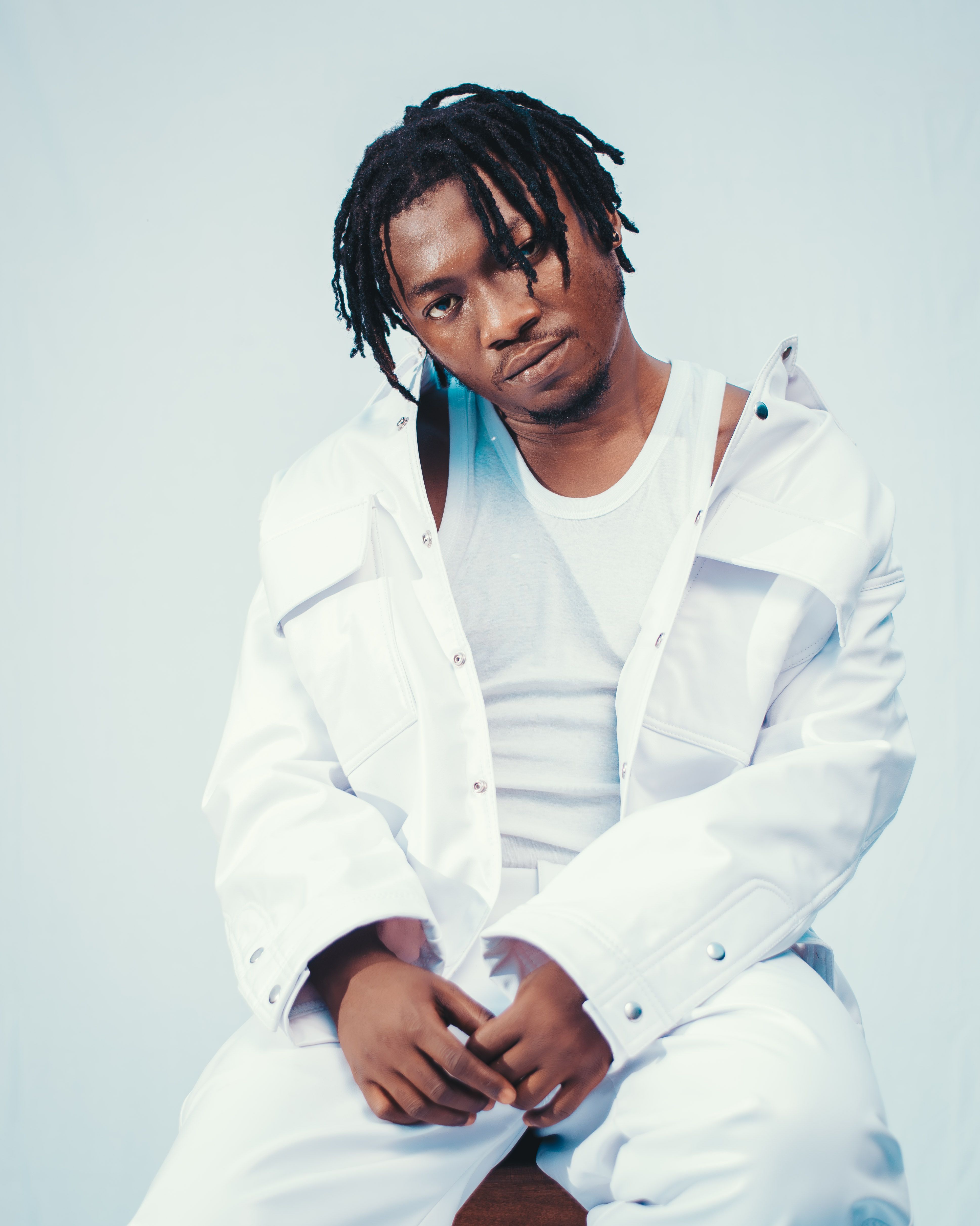 Studio portrait of an adult man wearing a white outfit with dreadlocks against a plain background.