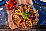 A vibrant seafood paella featuring octopus, shrimp, mussels, and fresh vegetables served outdoors.