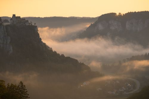 Free Enchanting clifftop castle amidst a misty valley at sunrise, perfect for travel inspiration. Stock Photo