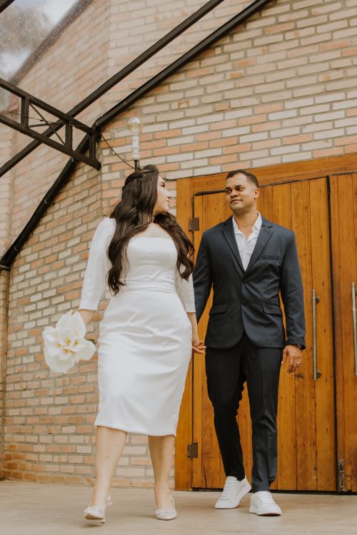 Free Stylish couple in wedding outfits walking hand in hand by a rustic brick wall. Stock Photo