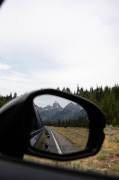 Scenic view of Grand Teton mountains reflected in a car side mirror during a rural drive