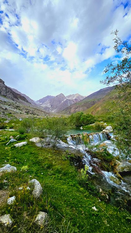 A stream flowing through a valley with mountains in the background ...