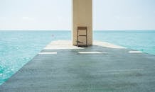 一张椅子坐在码头上，在明亮的天空下可以清晰地看到平静的海洋