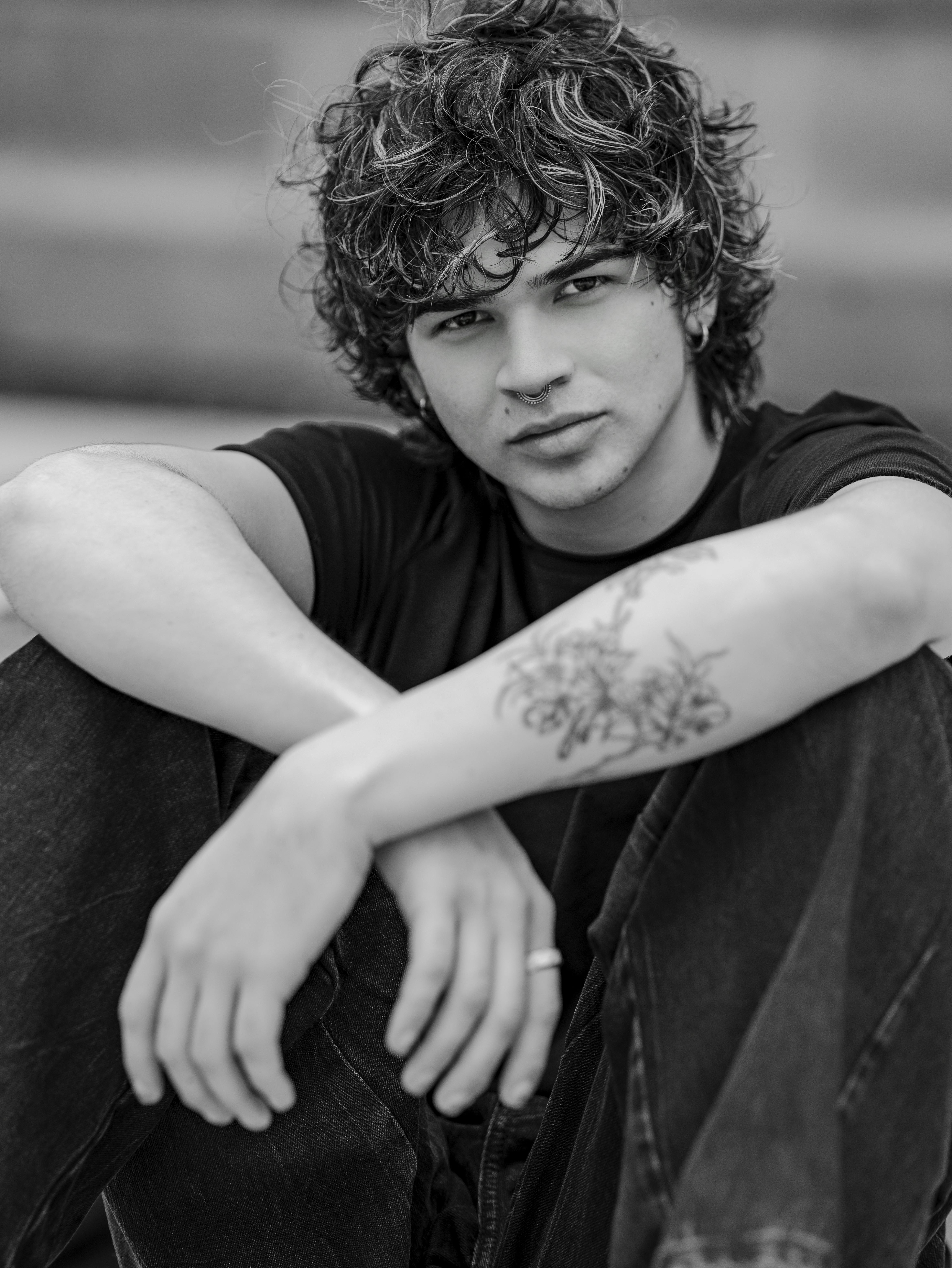 Black and white portrait of a young man sitting casually, dressed in jeans and a t-shirt.