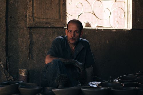 Free A thoughtful artisan potter sits surrounded by clay pots, showcasing traditional craftsmanship. Stock Photo
