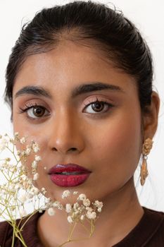 Close-up of a woman with elegant makeup and floral accent, exuding sophistication.