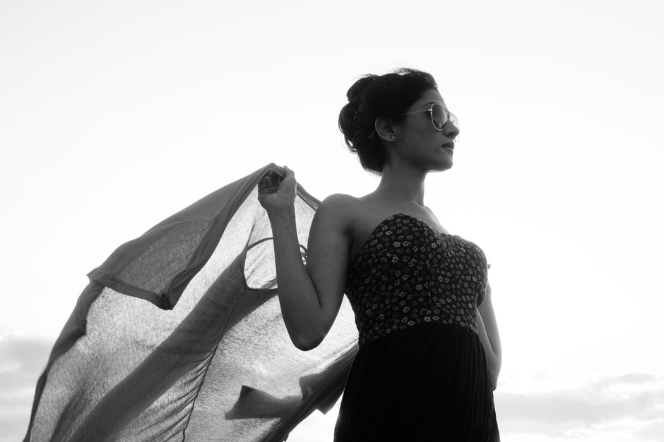 Elegant silhouette portrait of a young woman in sunglasses, capturing the essence of sunset with flowing fabric.