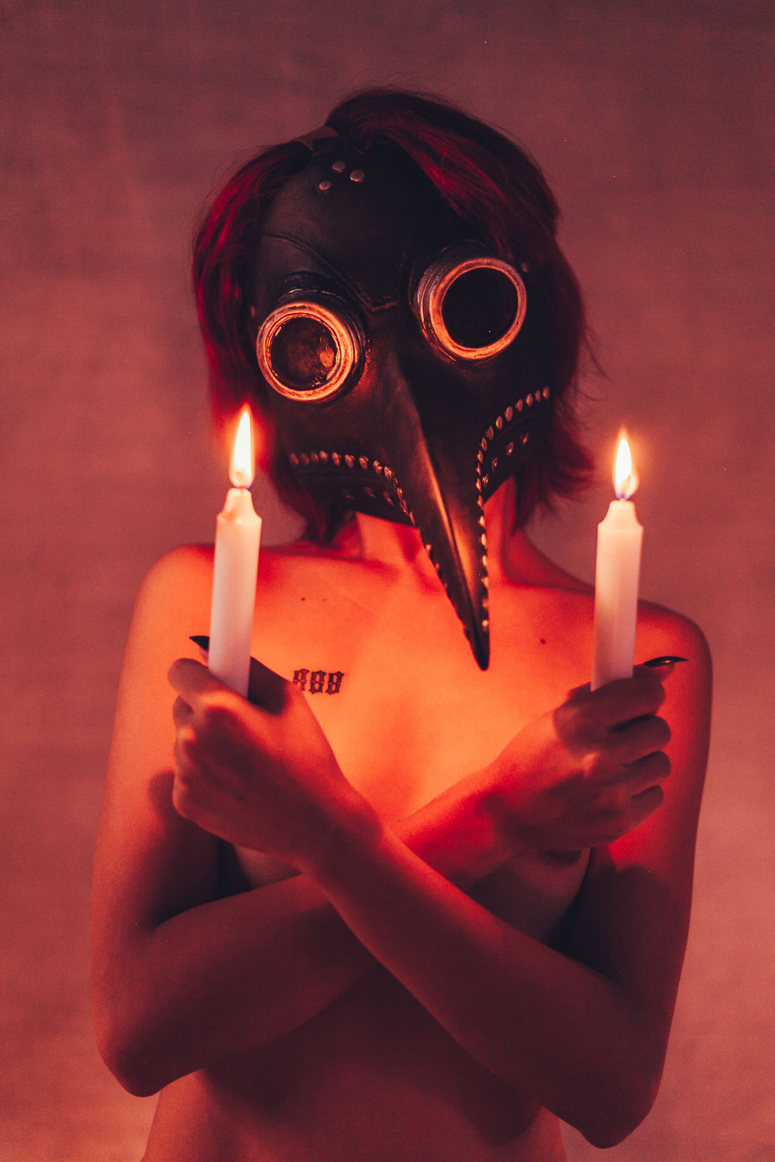 Artistic portrait of a person in a plague doctor mask holding candles in dim lighting.
