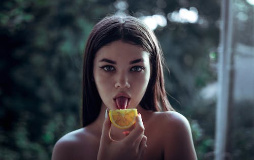 免费 女人舔橙色水果的选择性焦点摄影 素材图片
