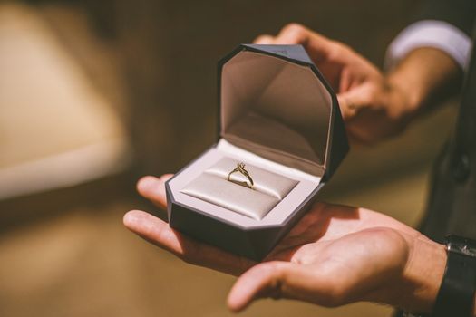 Close-up of an engagement ring in a box held by hands, symbolizing love and commitment.