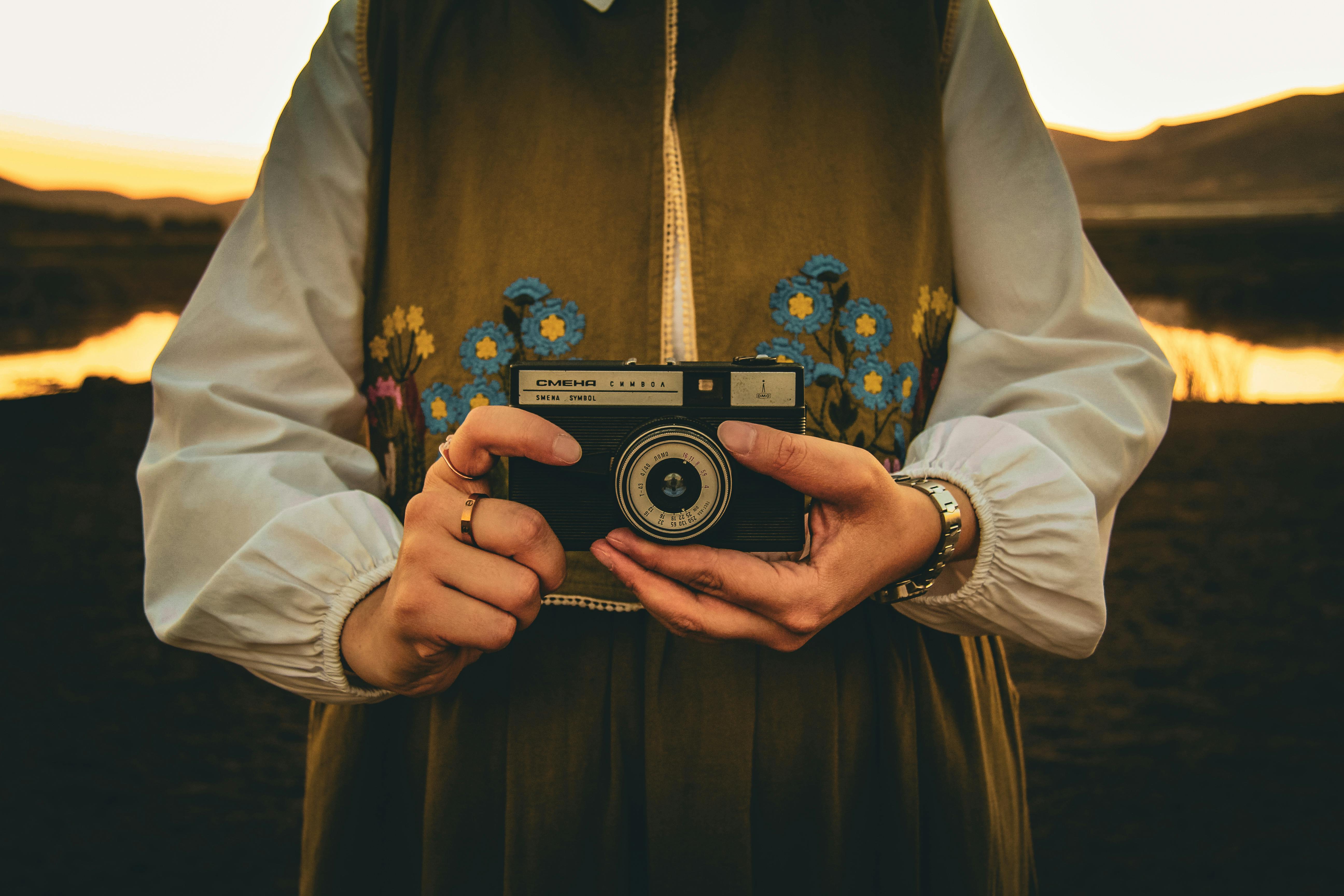 Close-up of a person holding a vintage camera against a sunset backdrop, capturing an artistic moment.