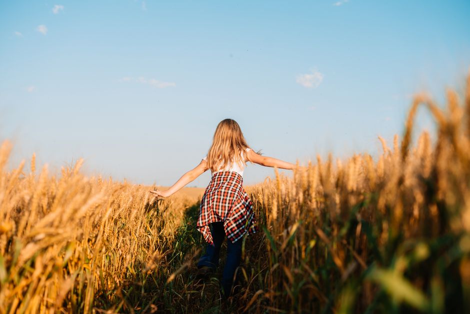 Una niña joven corre alegremente por un campo de trigo dorado bajo un cielo azul claro.
