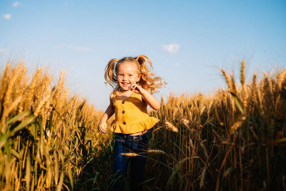 A young girl joyfully runs through a wheat field at sunset, enjoying the golden summer light.