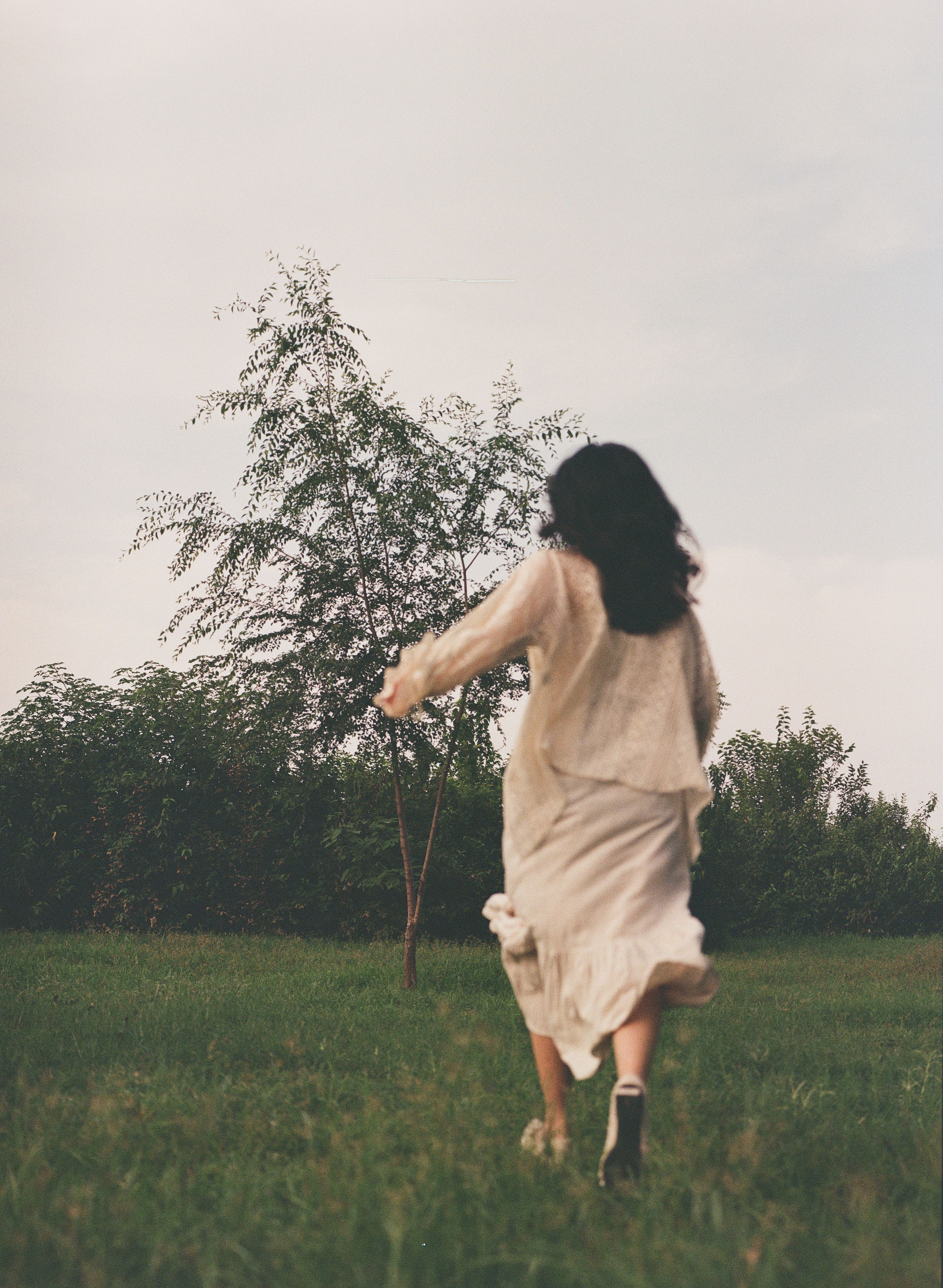 A woman in a white dress running through a field  Free Stock Photo