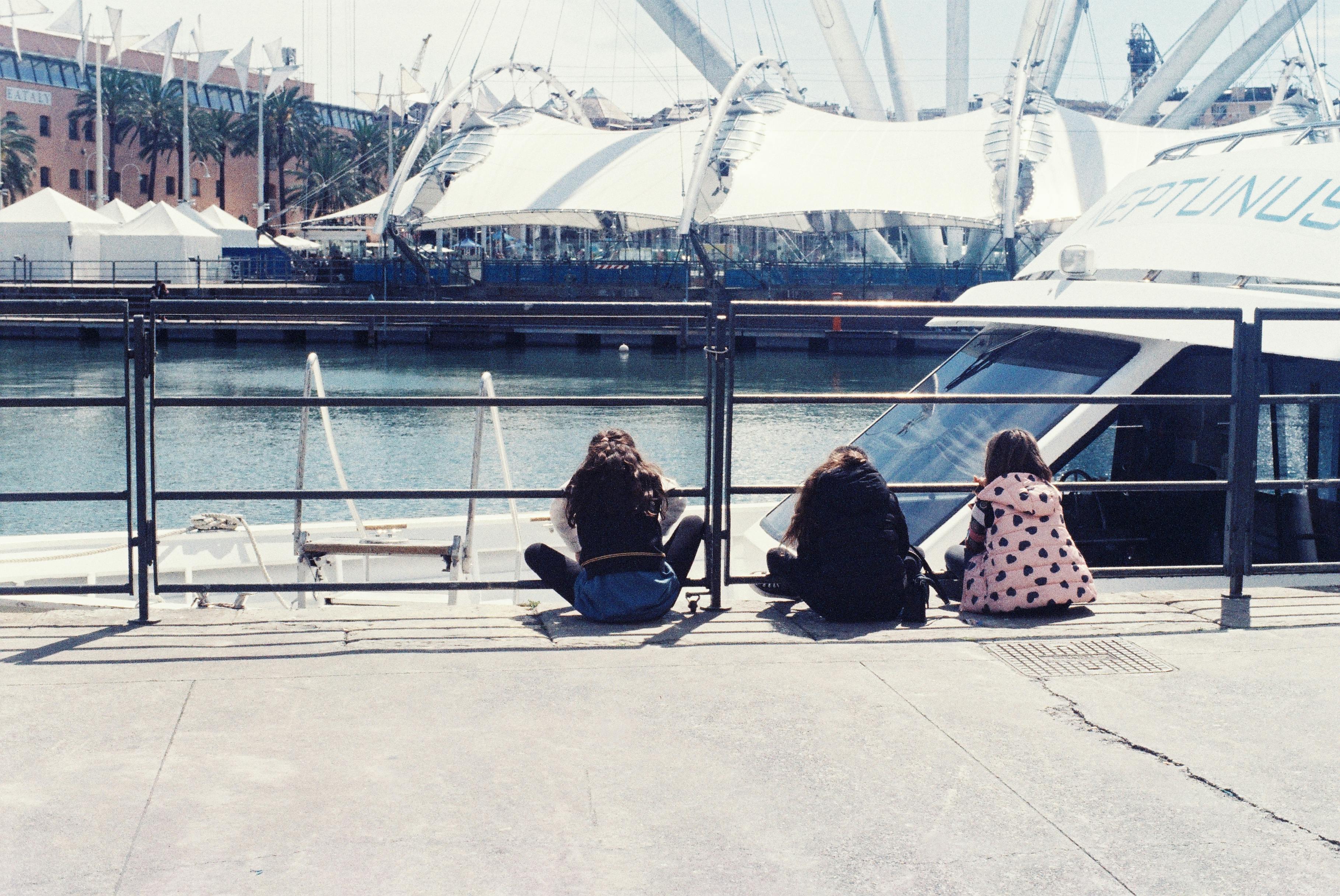 three people sitting on a bench near a boat