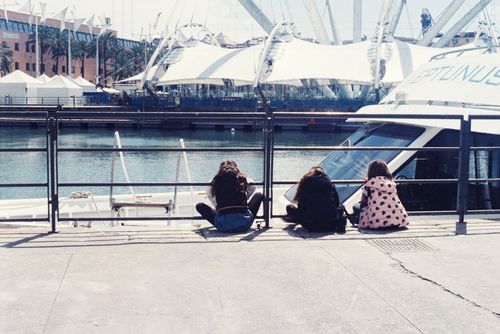Free Three young women sitting on a dock by a boat in an urban marina setting, enjoying a sunny day. Stock Photo