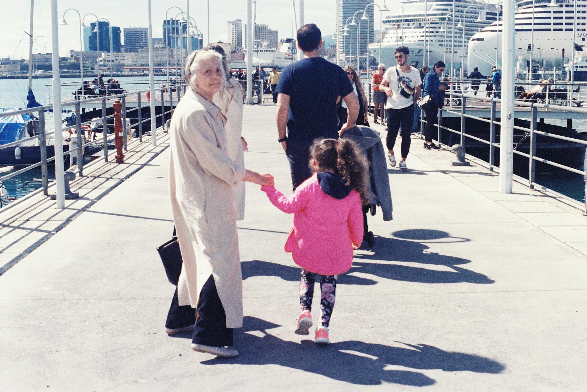 A family walks along a bustling city pier with cruise ships in the backdrop.