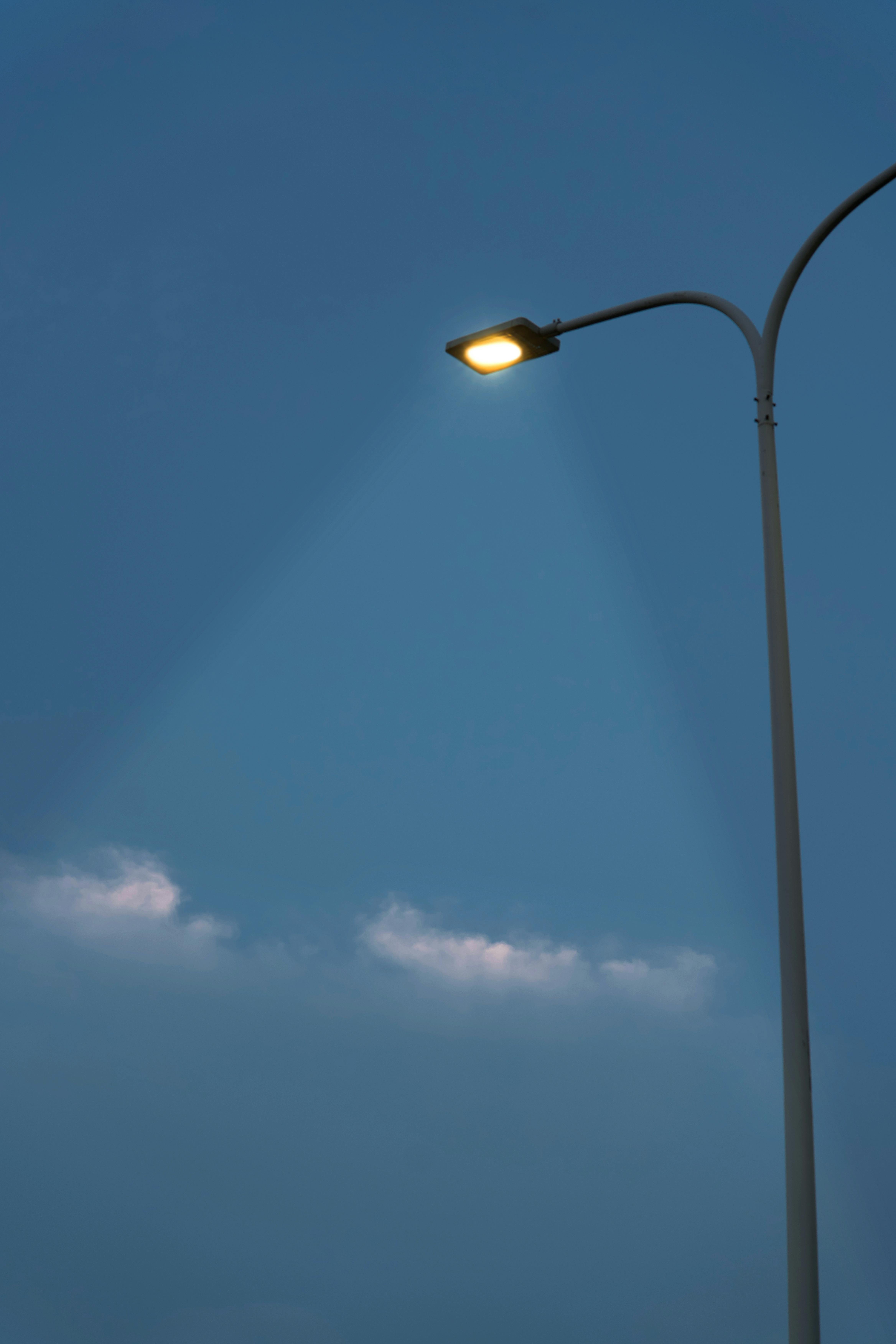 A single streetlamp shines brightly against a serene dusk sky with scattered clouds.