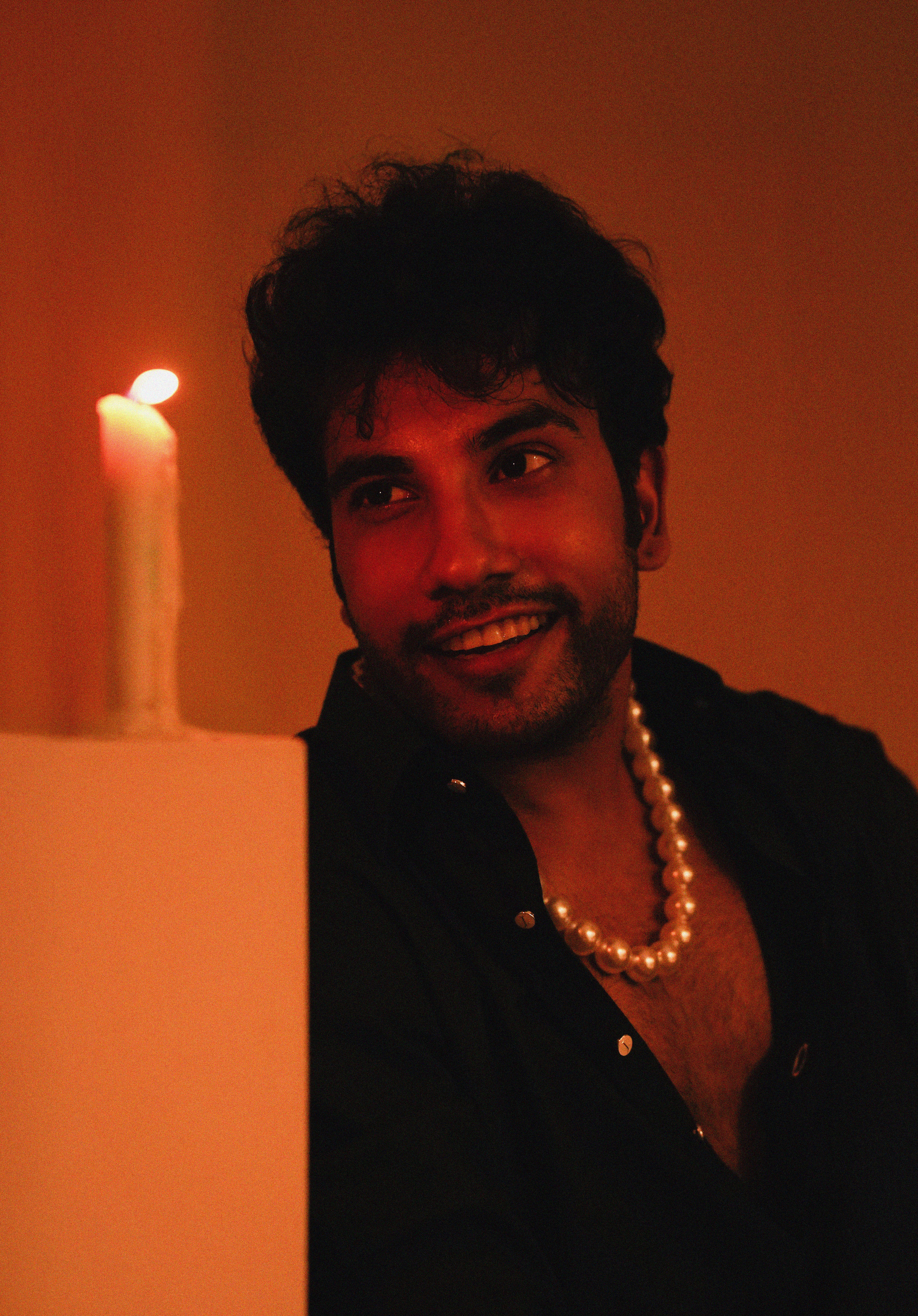 Moody portrait of a man with pearls, illuminated by candlelight.