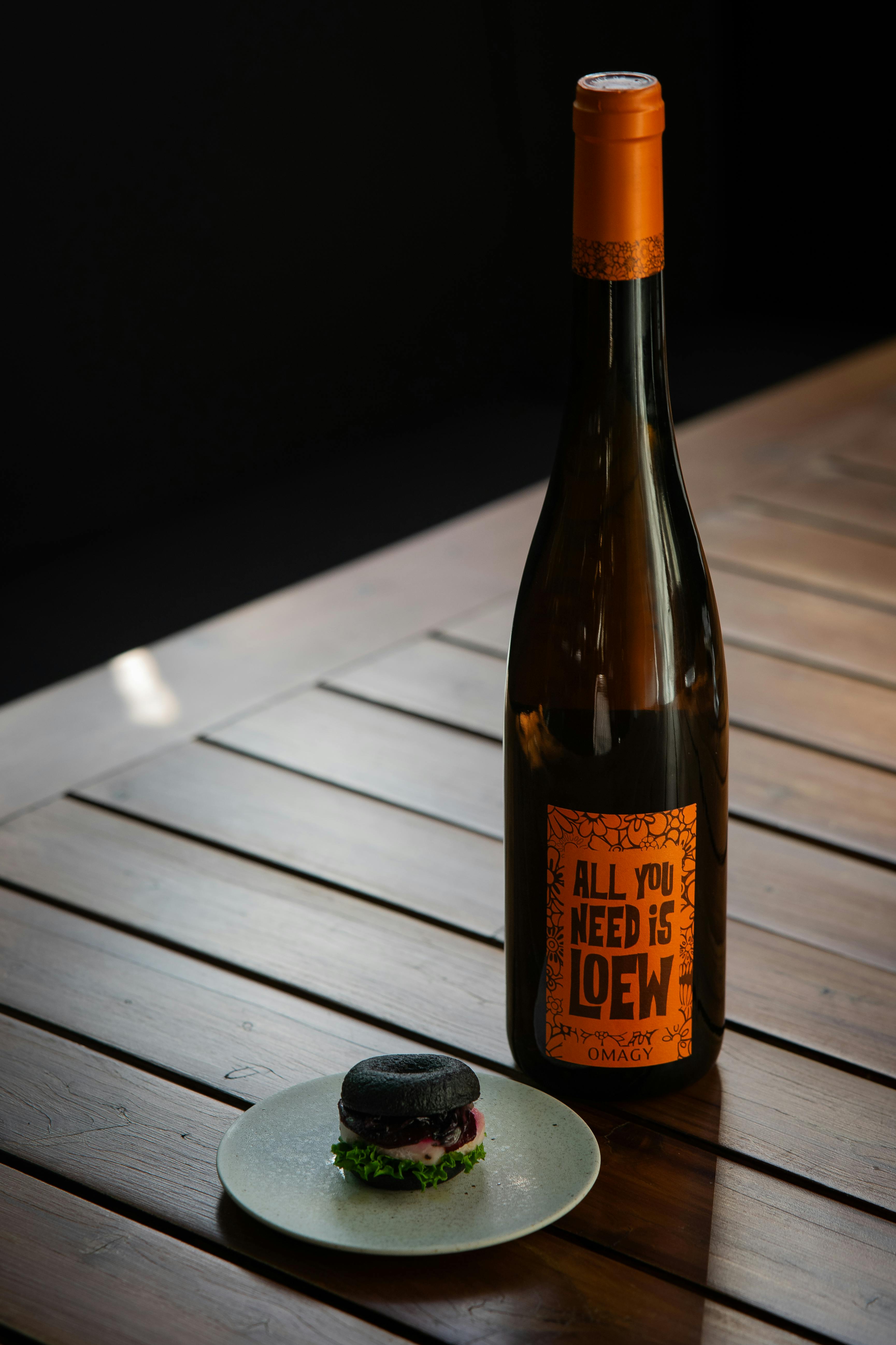 A rustic still life image of a wine bottle and gourmet burger on a wooden table, indoors.