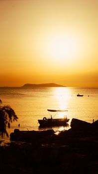 Silhouette of boats on calm waters during a stunning golden sunset by the sea.