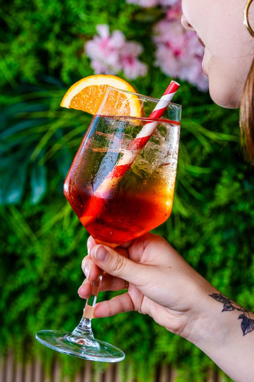 Free Vibrant iced cocktail with orange garnish in a lush garden atmosphere, perfect for summer. Stock Photo
