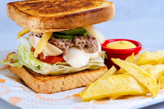 Delicious sandwich with lettuce, cheese, and fries on a colorful table setting.