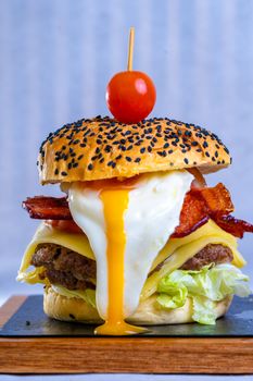 Delicious gourmet burger with bacon, cheese, egg, and a cherry tomato on a sesame bun.
