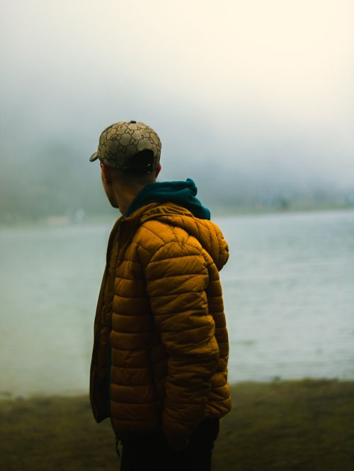 Free A man in a yellow jacket stands by a misty lake, showcasing a serene autumn evening. Stock Photo